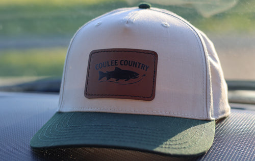 Coulee Country Bend Hat in Dark Green / Natural / Light Brown patch, natural crown with dark green brim and leather trout patch, on a truck dashboard